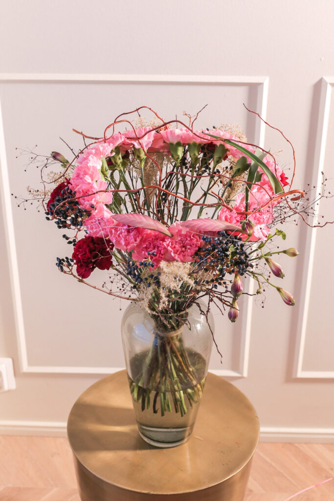 vaaleanpunaisia neilikoita aseteltu ympyränmuotoiseksi lasimaljakossa pöydällä